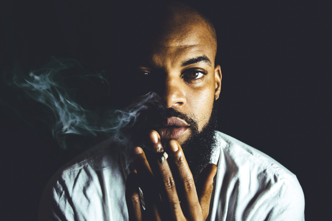 The Exotic Smoker Vape and Smoke Shop - Augusta - Georgia - Black Man with a Beard Holding a Hemp Blunt with Rising Smoke