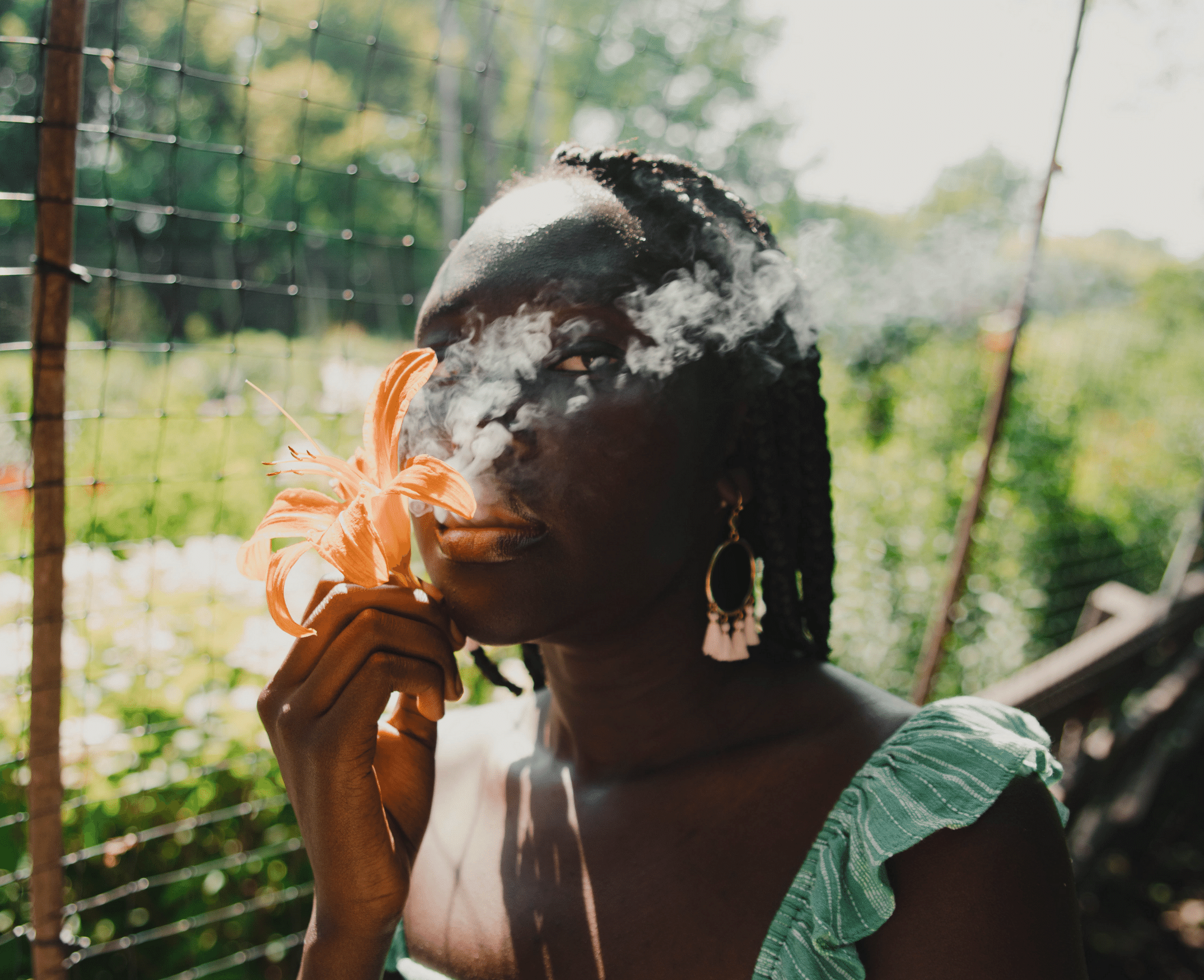 The Exotic Smoker Vape and Smoke Shop - Augusta - Georgia - Smoke plumes behind an orange flower and a dark skinned woman with gold earing. 