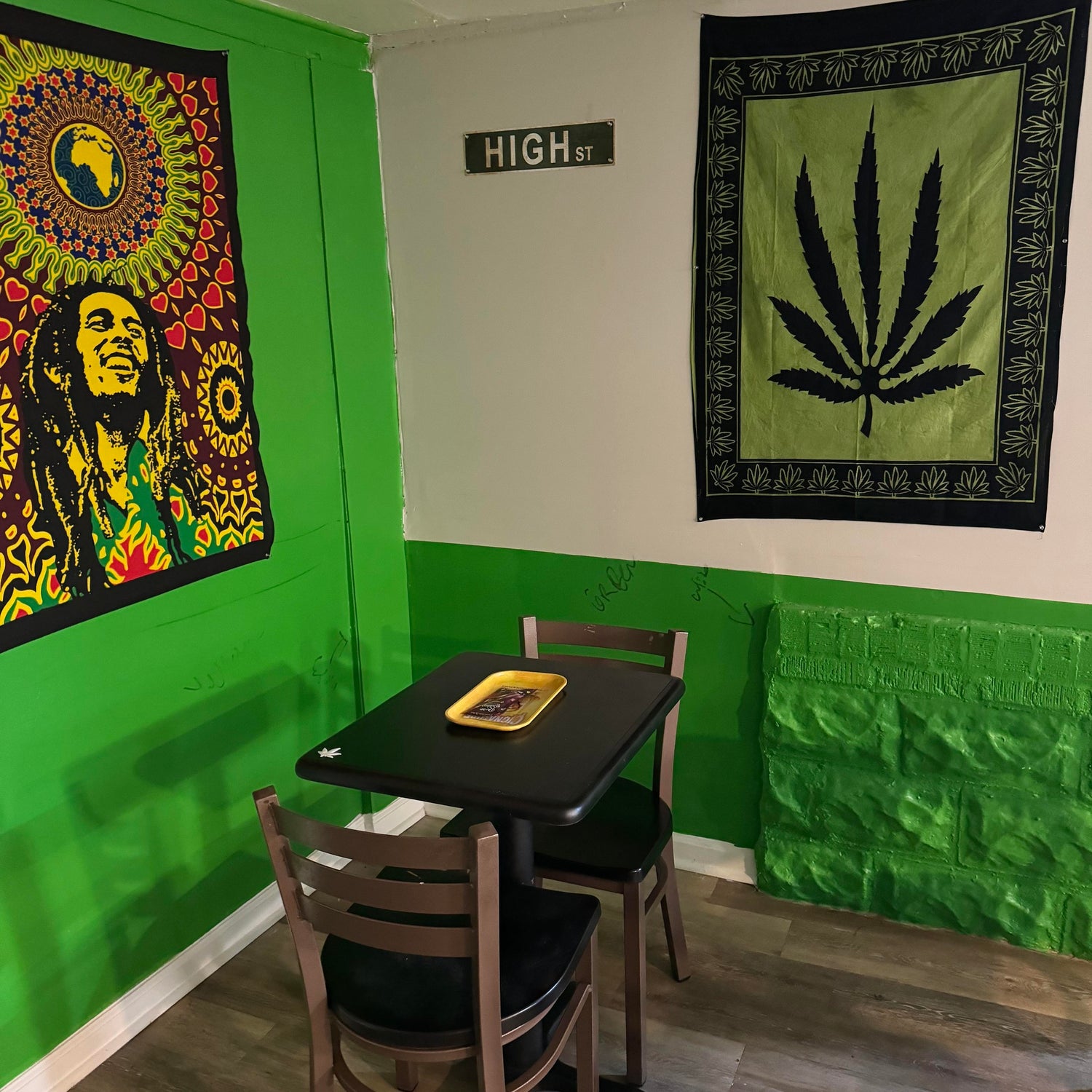 The Exotic Smoker Vape and Smoke Shop - Rental Venue 4 - Tabel and chairs with bob marly imagery and a hemp leaf on the wall with a high street sign